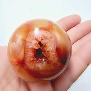 carnelian sphere, crystal, gemstone, polished, different shades of orange, has a natural hole in it