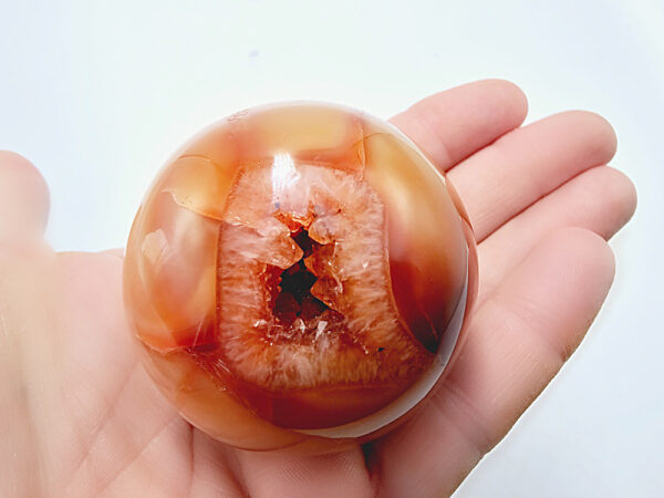 carnelian sphere, crystal, gemstone, polished, different shades of orange, has a natural hole in it